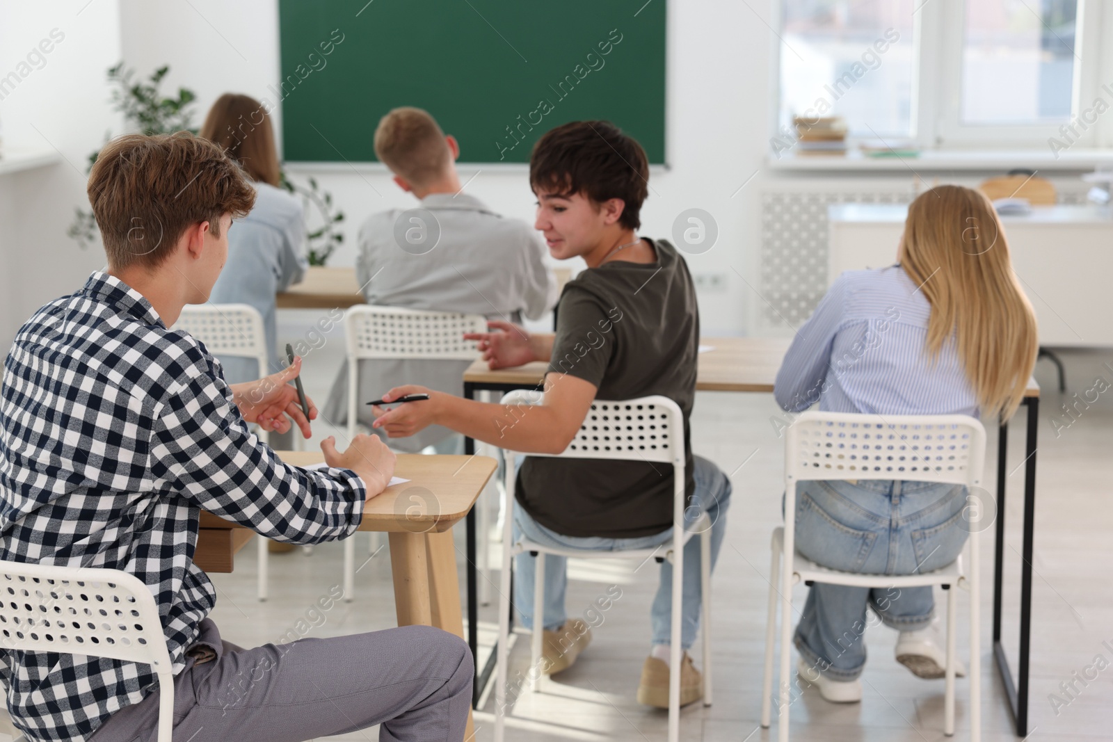 Photo of Students taking exam at wooden table indoors