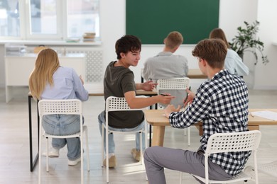 Photo of Students taking exam at wooden table indoors