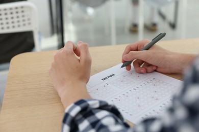 Photo of Student filling out answer sheet at wooden table indoors, closeup. Taking exam