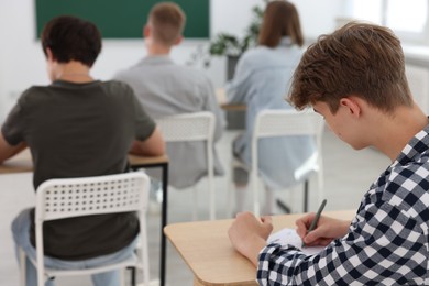 Photo of Students taking exam at wooden table indoors, selective focus
