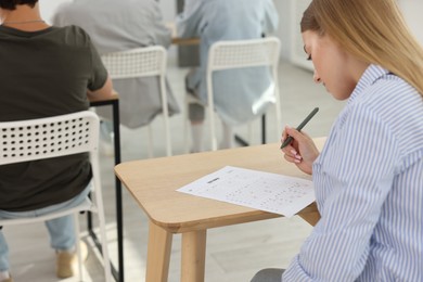 Photo of Students taking exam at wooden table indoors, selective focus