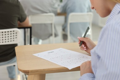 Photo of Student filling out answer sheet at wooden table indoors, closeup. Taking exam