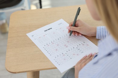 Photo of Student filling out answer sheet at wooden table indoors, closeup. Taking exam