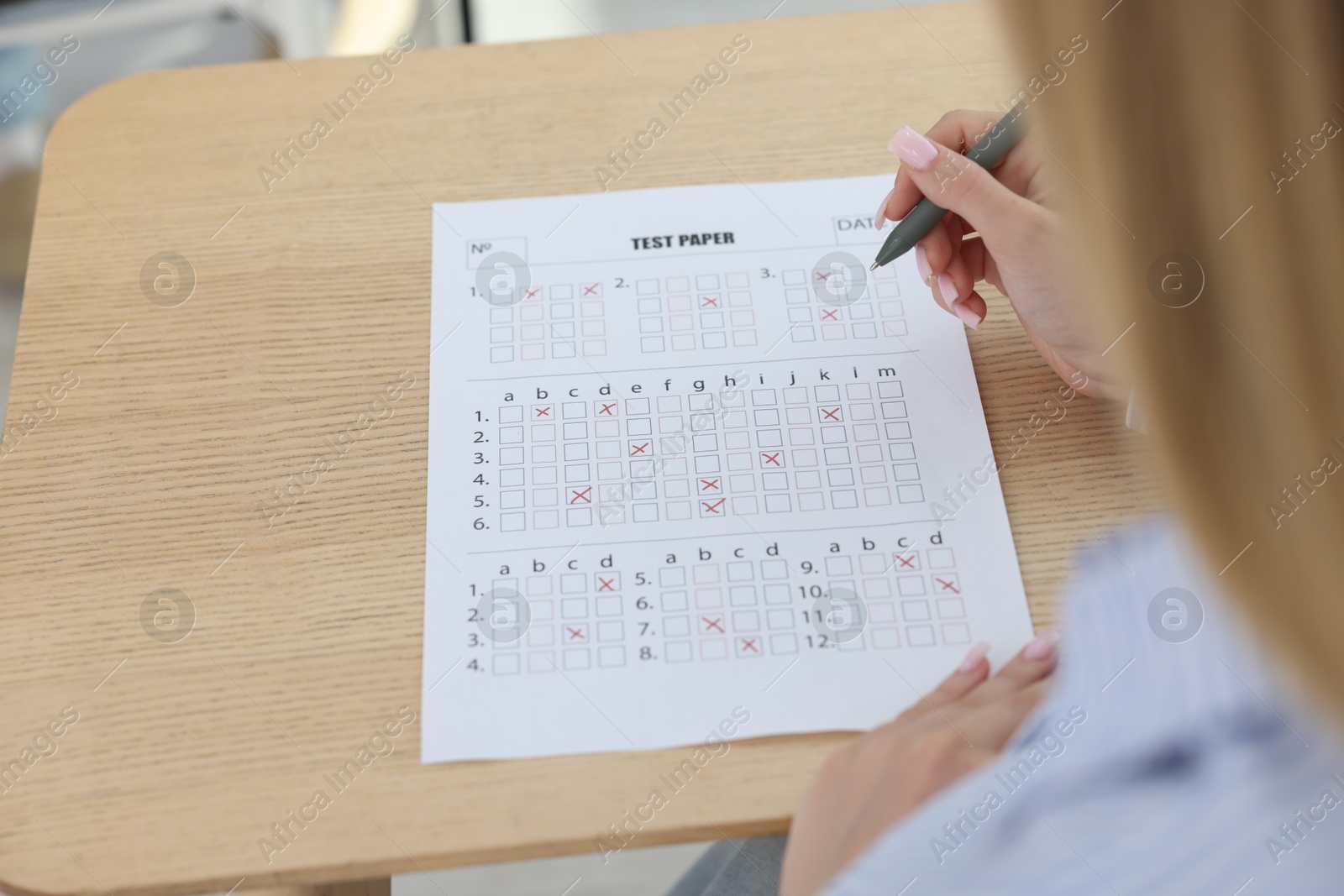 Photo of Student filling out answer sheet at wooden table indoors, closeup. Taking exam