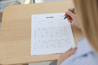 Photo of Student filling out answer sheet at wooden table indoors, closeup. Taking exam