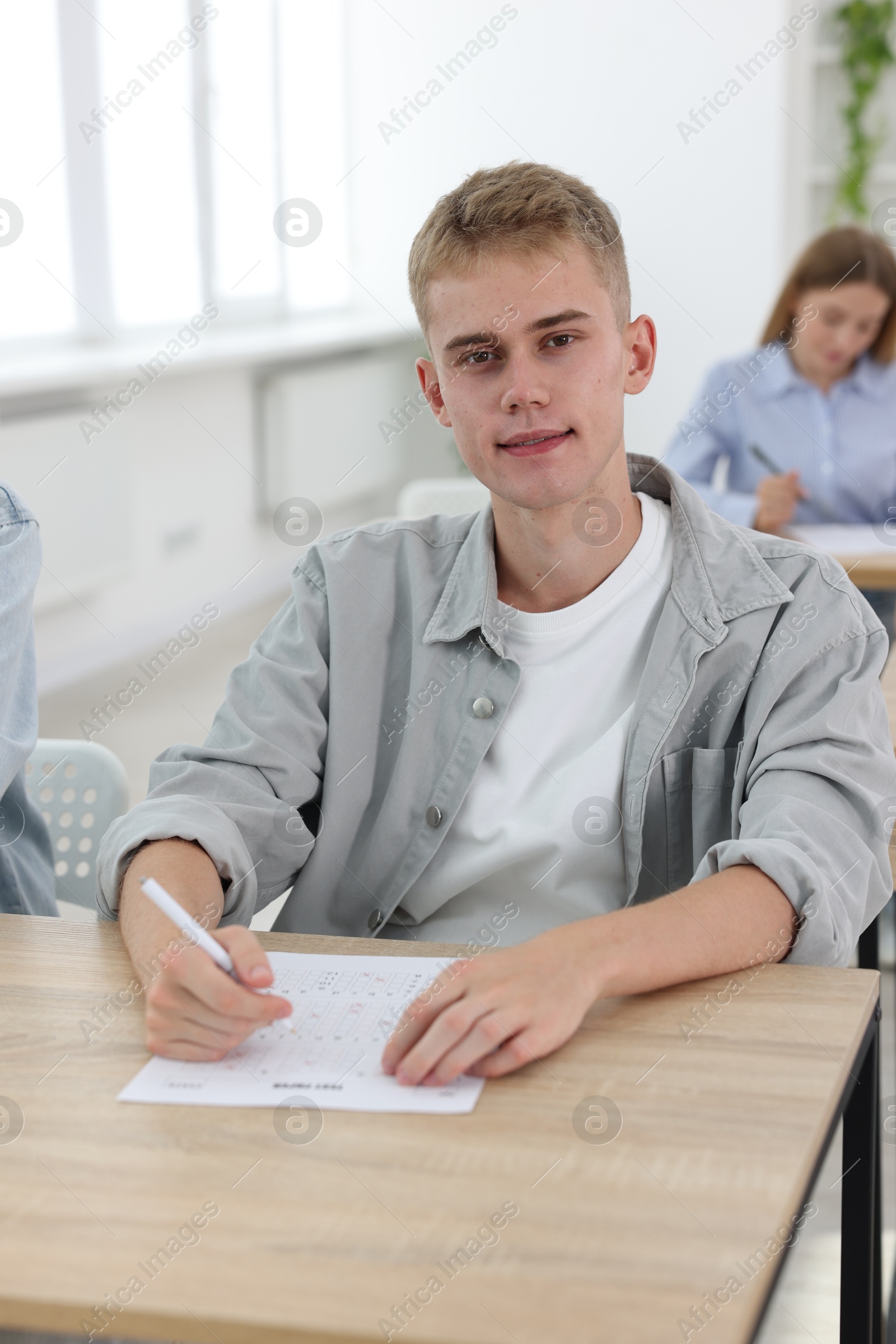Photo of Student taking exam at wooden table indoors