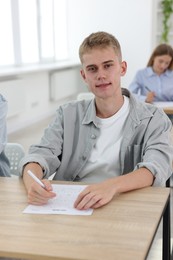 Photo of Student taking exam at wooden table indoors