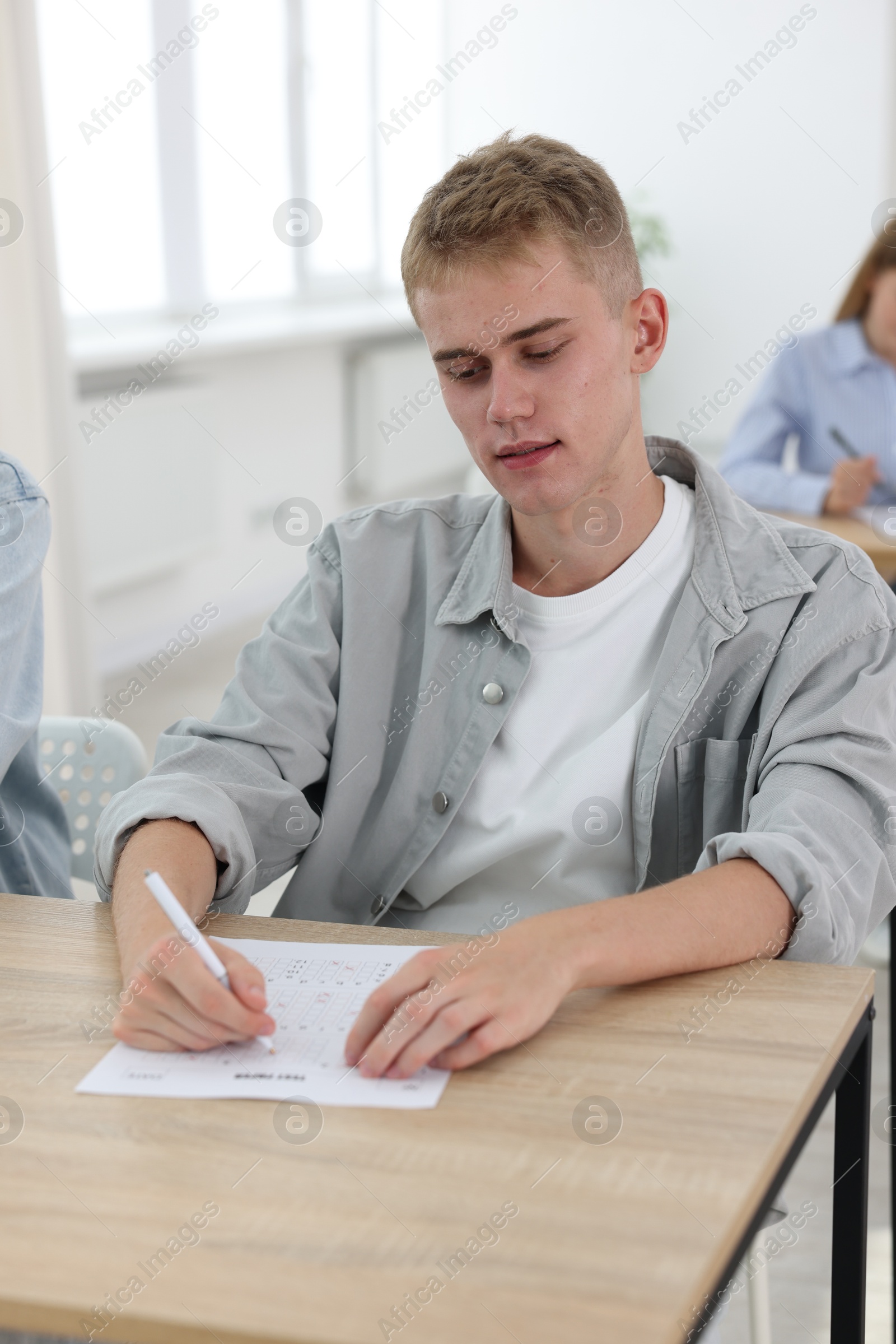 Photo of Student taking exam at wooden table indoors