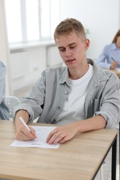 Photo of Student taking exam at wooden table indoors