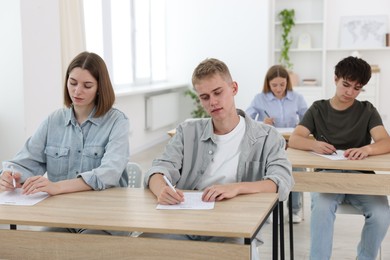 Photo of Students taking exam at wooden table indoors
