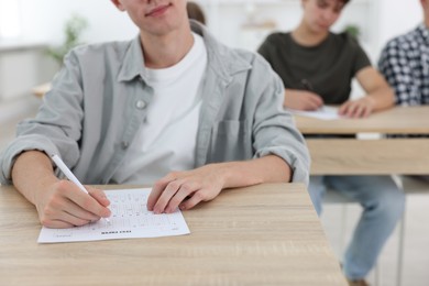 Photo of Students taking exam at wooden table indoors, selective focus