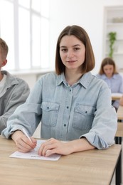Photo of Students taking exam at wooden table indoors, selective focus