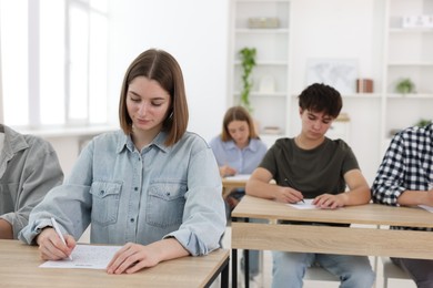 Photo of Students taking exam at wooden table indoors, selective focus