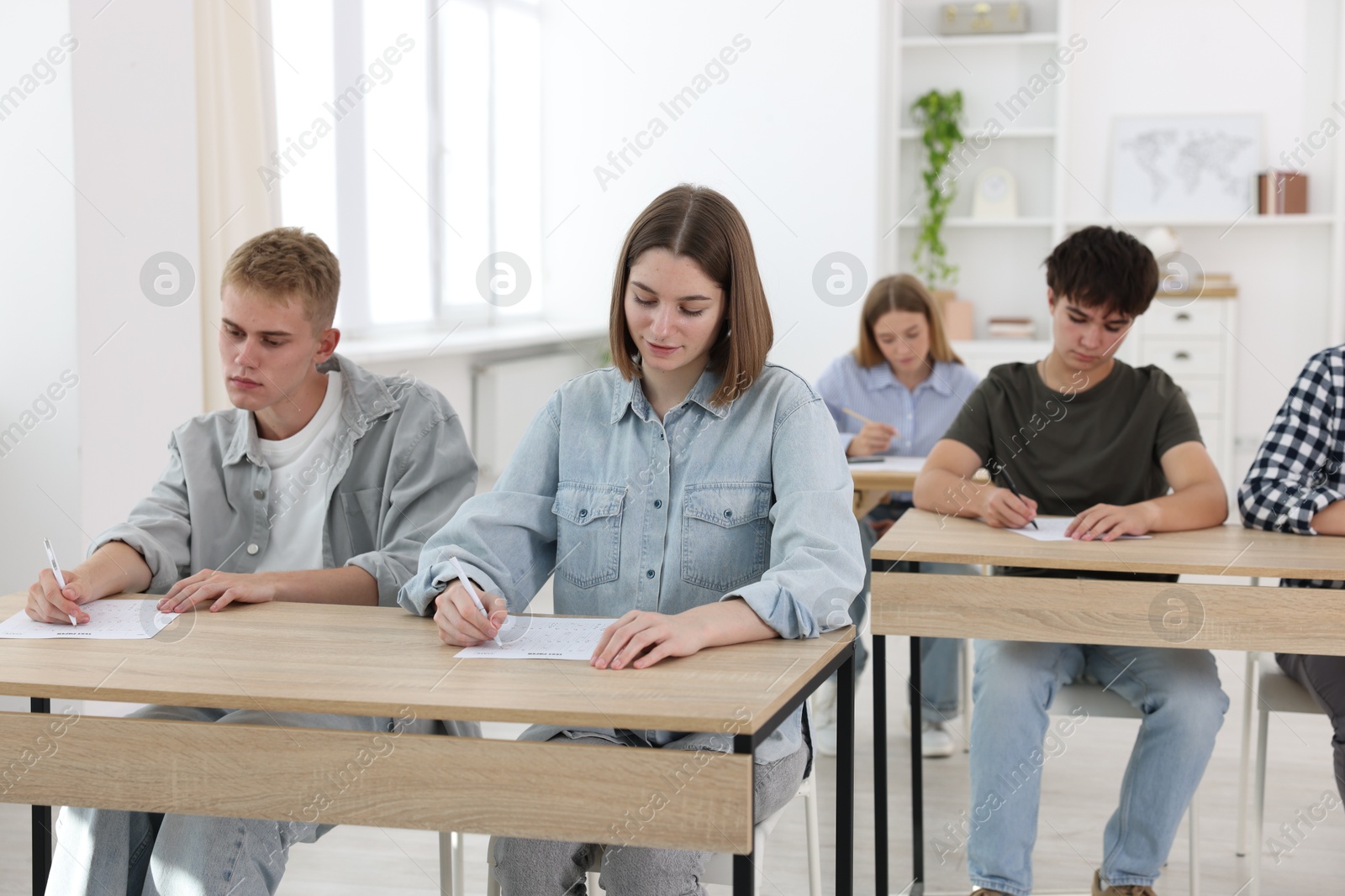 Photo of Students taking exam at wooden table indoors