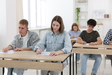 Photo of Students taking exam at wooden table indoors