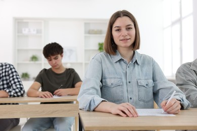 Photo of Students taking exam at wooden table indoors, selective focus