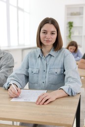 Photo of Students taking exam at wooden table indoors, selective focus