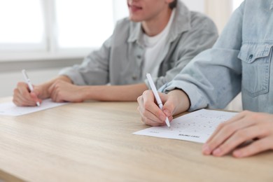 Photo of Students filling out answer sheet at wooden table indoors, closeup. Taking exam