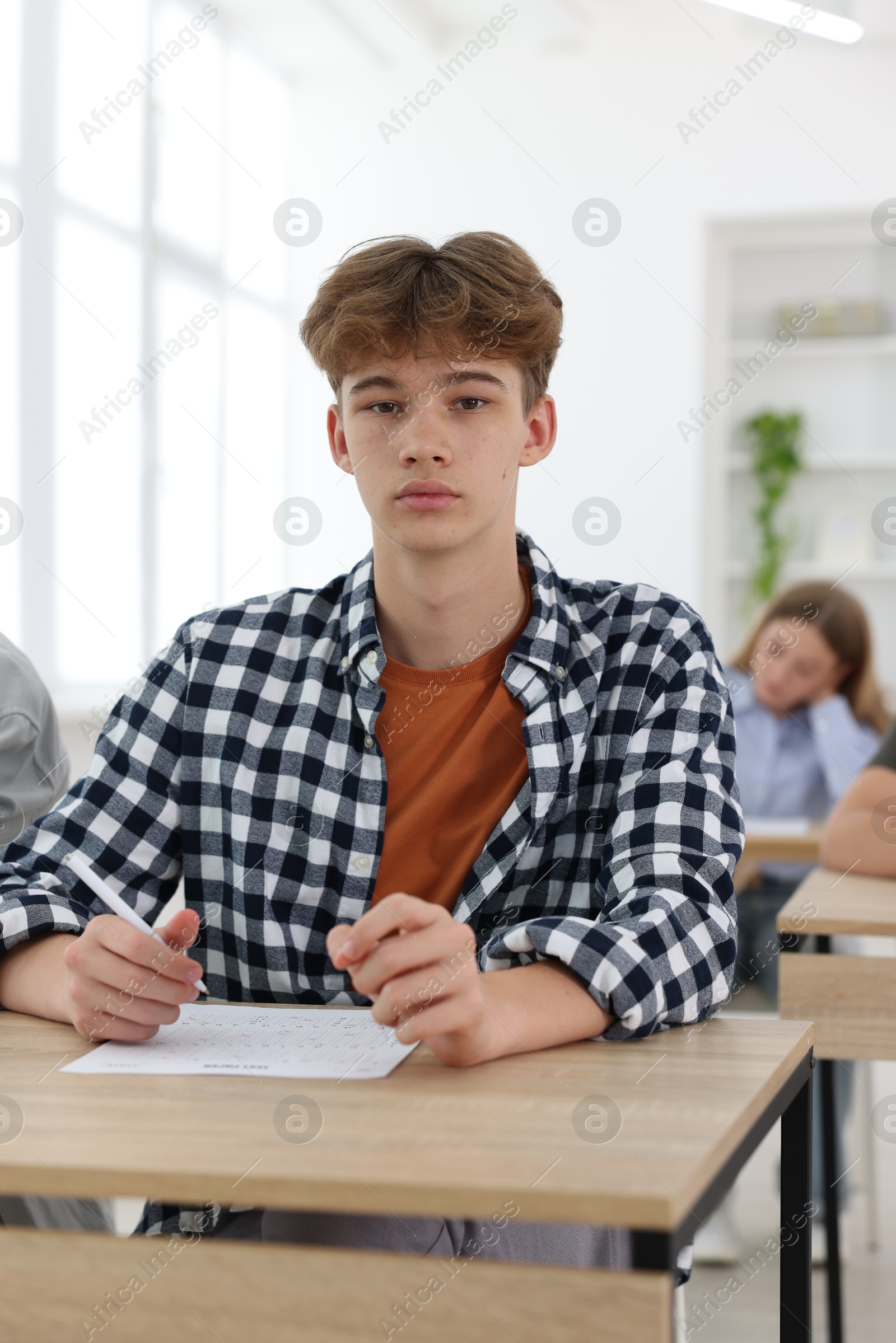 Photo of Students taking exam at wooden table indoors, selective focus
