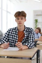 Photo of Students taking exam at wooden table indoors, selective focus
