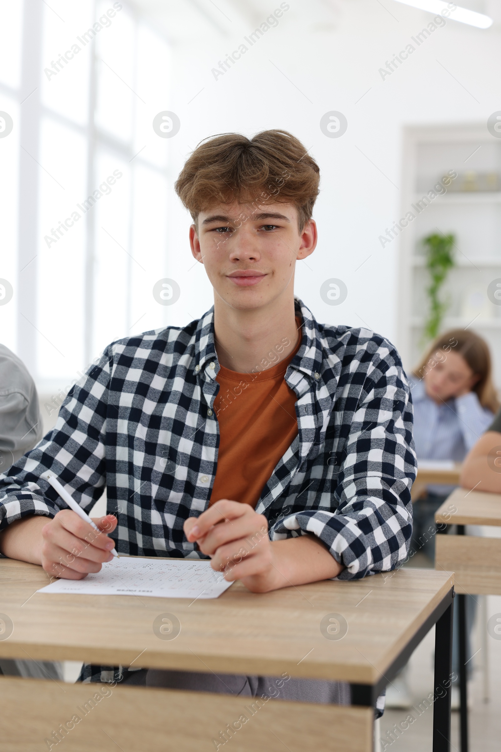 Photo of Students taking exam at wooden table indoors, selective focus