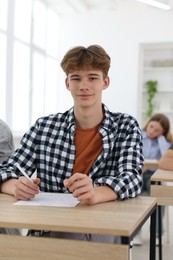 Photo of Students taking exam at wooden table indoors, selective focus
