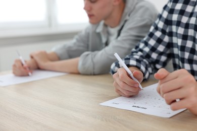 Photo of Students taking exam at wooden table indoors, selective focus