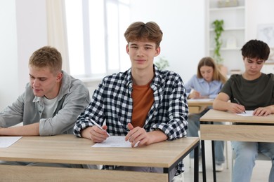 Photo of Students taking exam at wooden table indoors