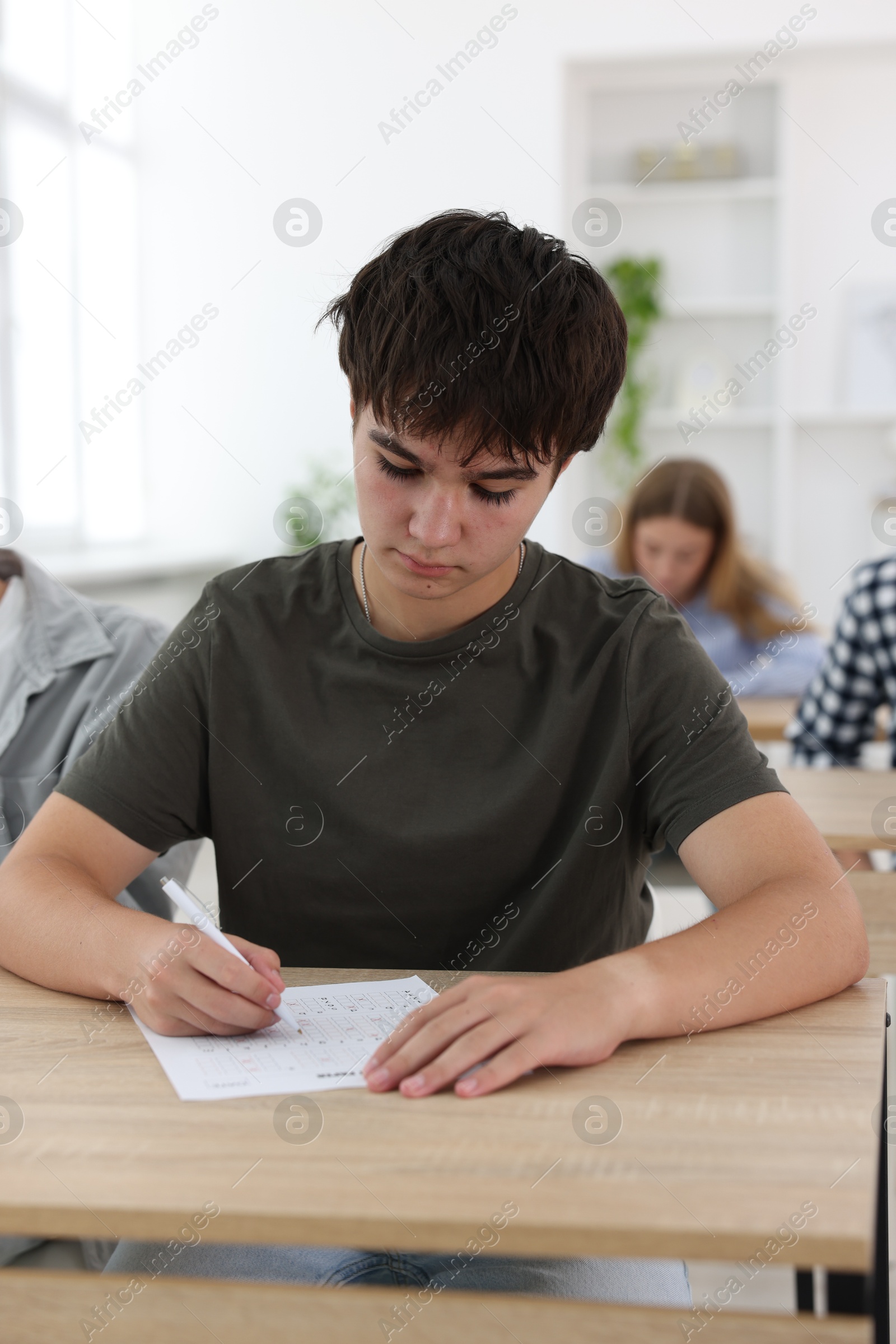 Photo of Students taking exam at wooden table indoors, selective focus