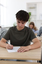 Photo of Students taking exam at wooden table indoors, selective focus