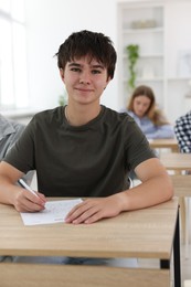 Photo of Students taking exam at wooden table indoors, selective focus