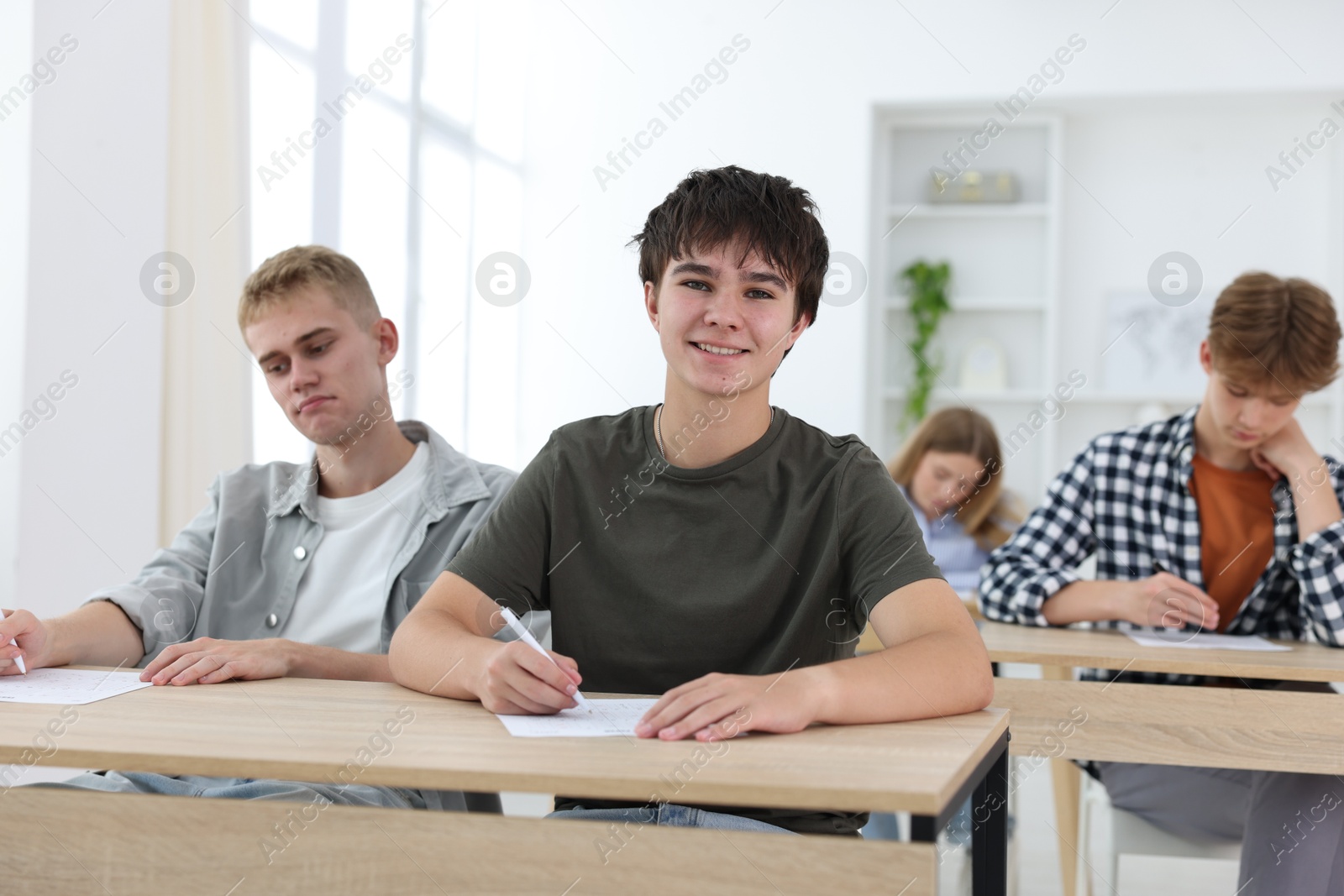 Students taking exam at wooden table indoors, selective focus Photo of Students taking exam at wooden table indoors, selective focus