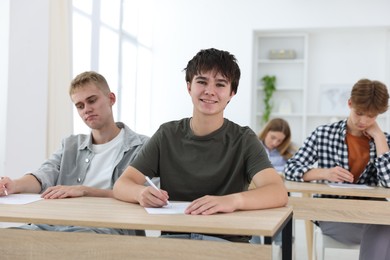 Photo of Students taking exam at wooden table indoors, selective focus