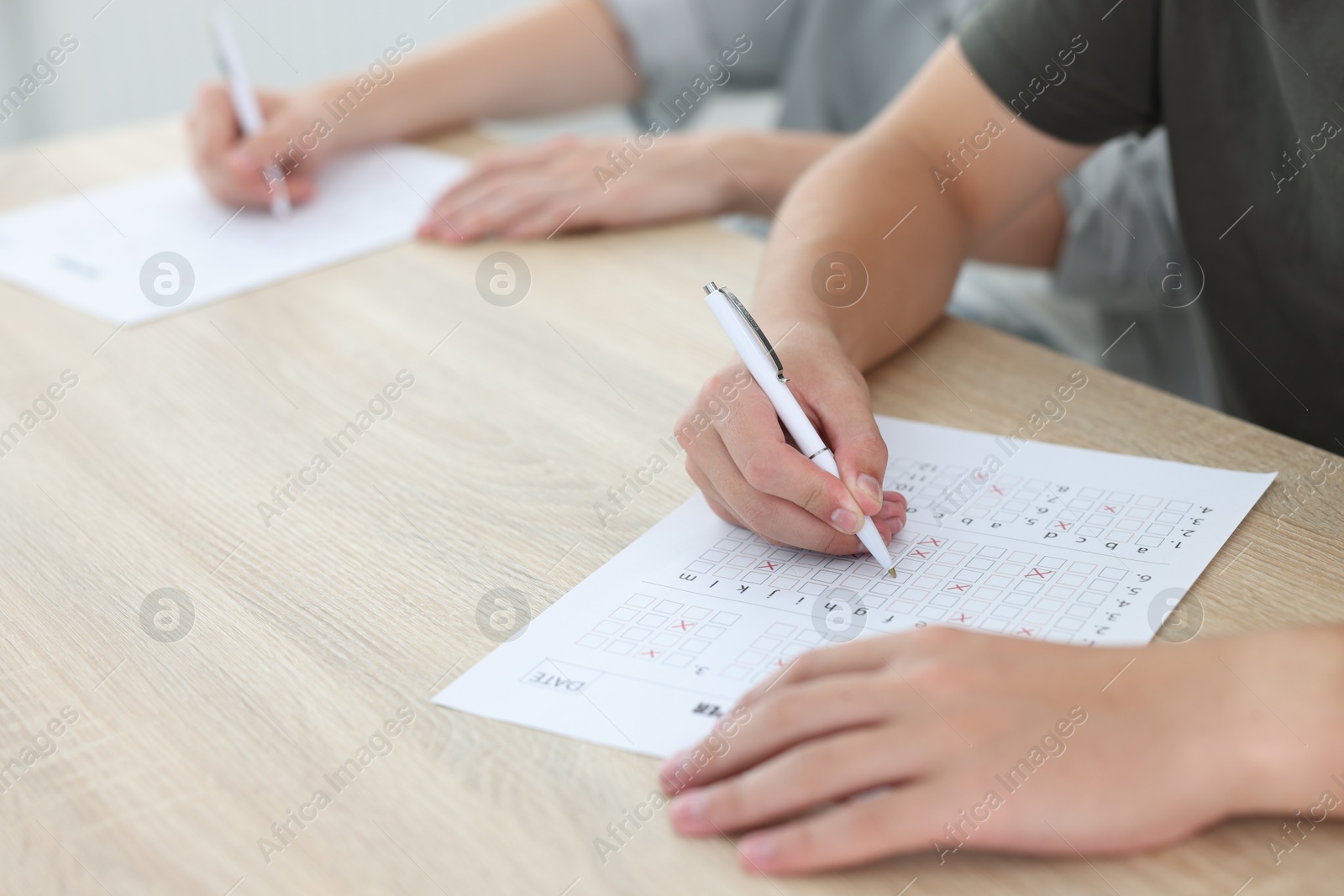 Photo of Students filling out answer sheet at wooden table indoors, closeup. Taking exam