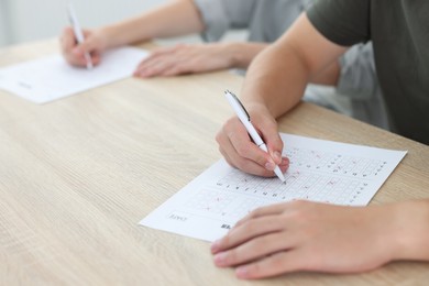 Photo of Students filling out answer sheet at wooden table indoors, closeup. Taking exam