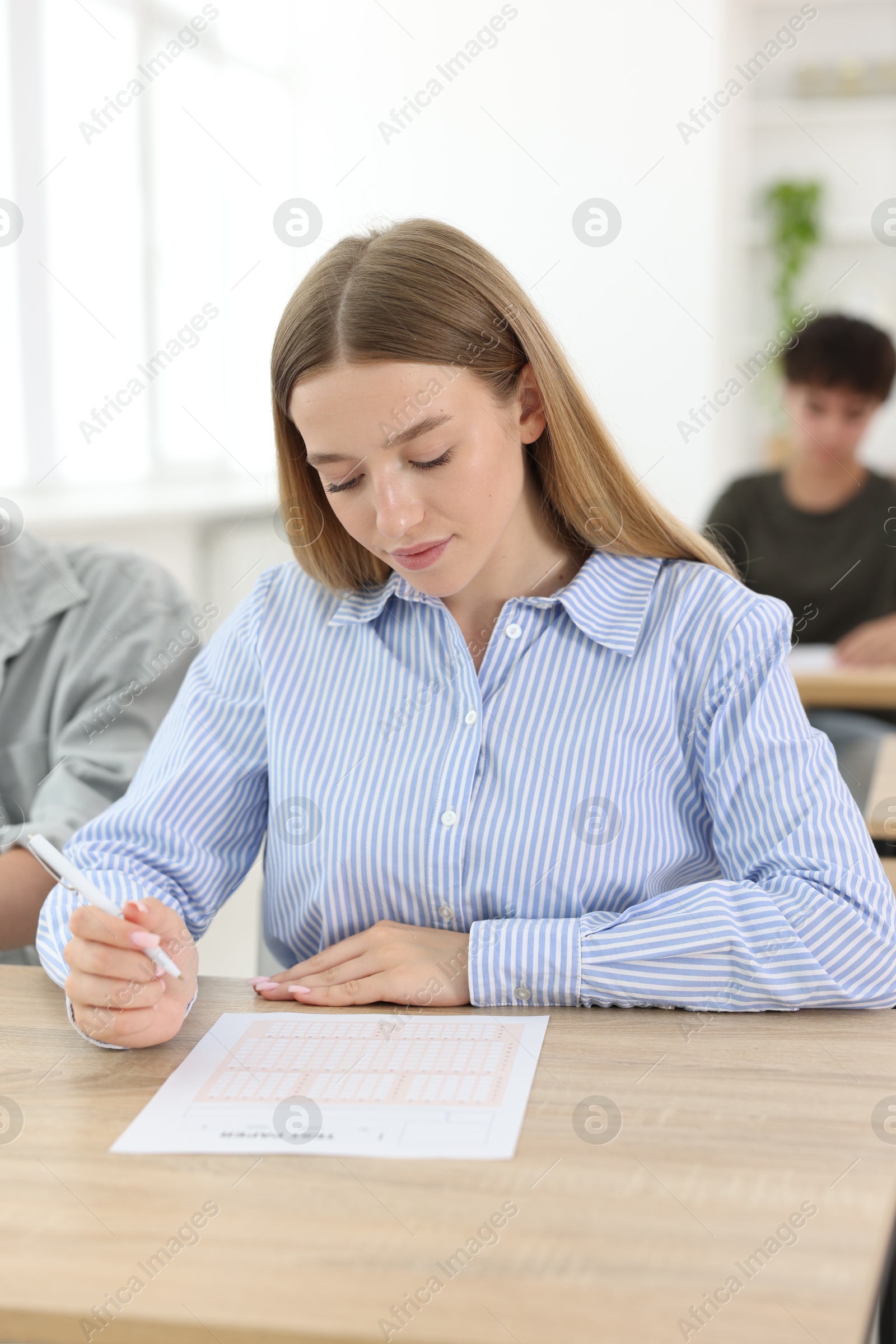 Photo of Students taking exam at wooden table indoors, selective focus