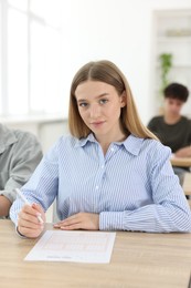 Photo of Students taking exam at wooden table indoors, selective focus