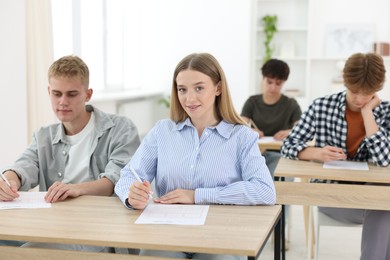 Photo of Students taking exam at wooden table indoors