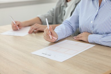 Photo of Students filling out answer sheet at wooden table indoors, closeup. Taking exam