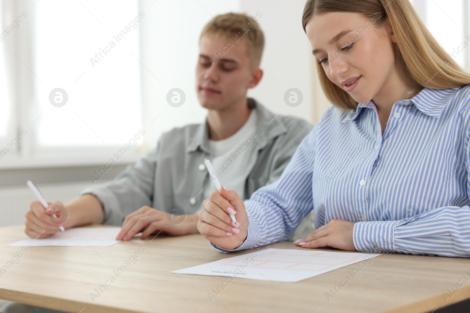 Photo of Students taking exam at wooden table indoors, selective focus