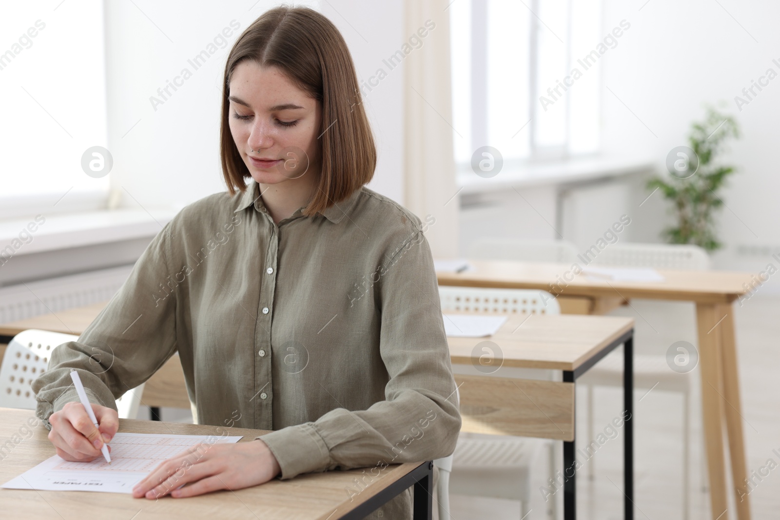 Photo of Student taking exam at wooden table indoors. Space for text