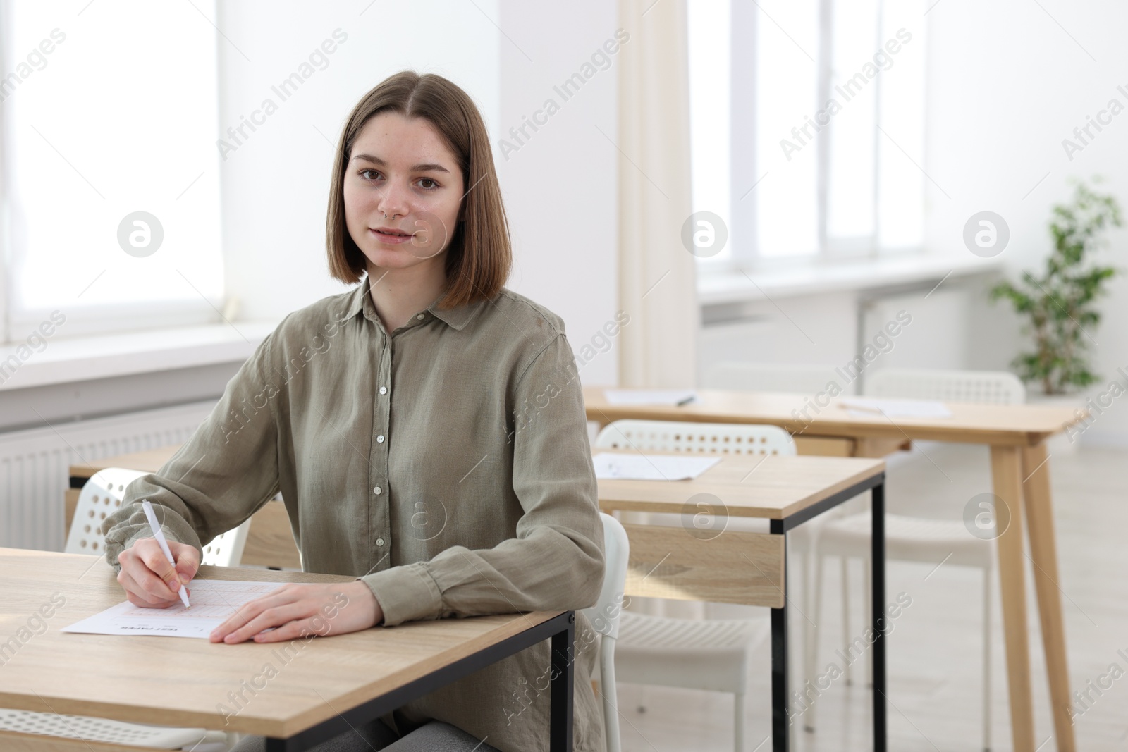 Photo of Student taking exam at wooden table indoors. Space for text