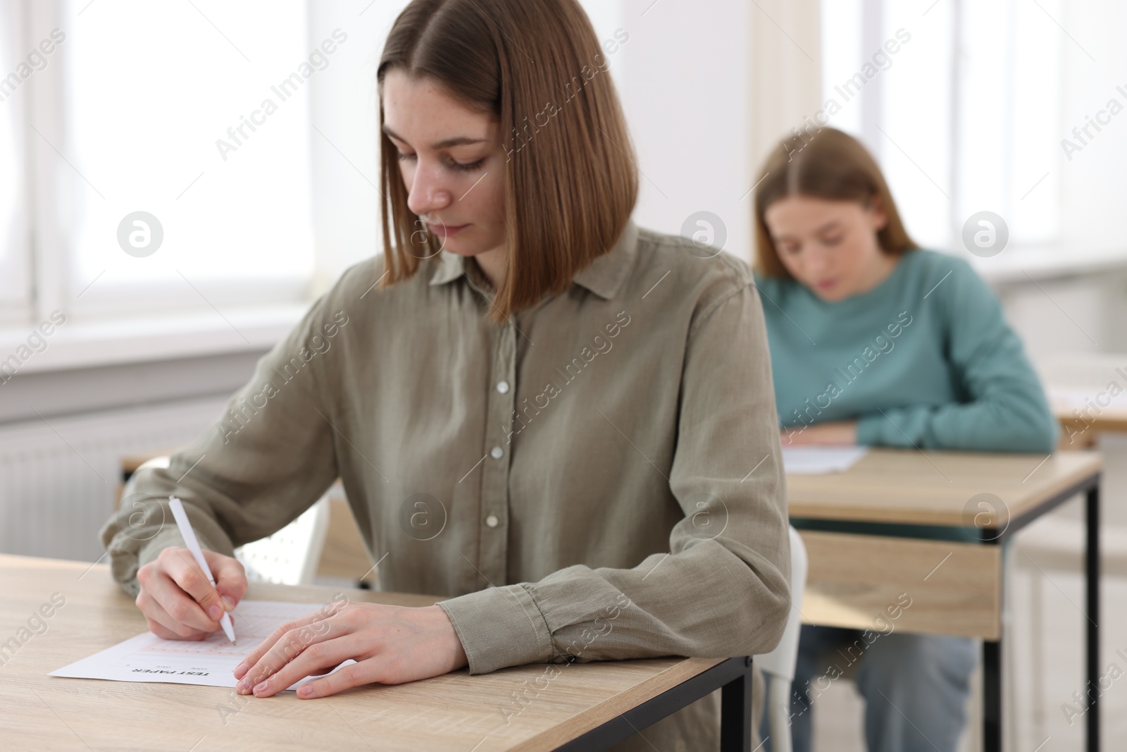 Photo of Students taking exam at wooden table indoors, selective focus