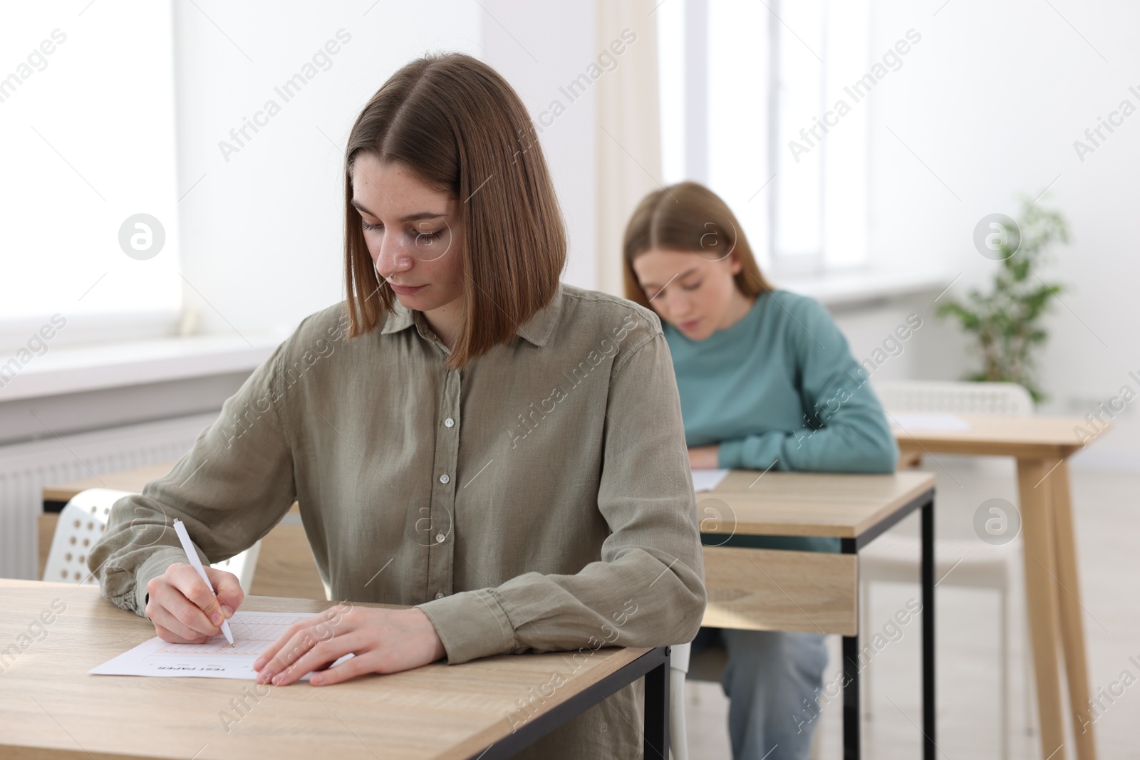 Photo of Students taking exam at wooden table indoors, selective focus