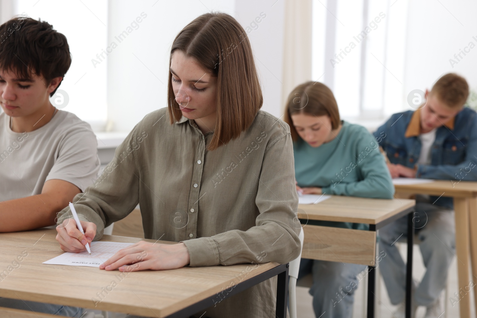 Photo of Students taking exam at wooden table indoors, selective focus
