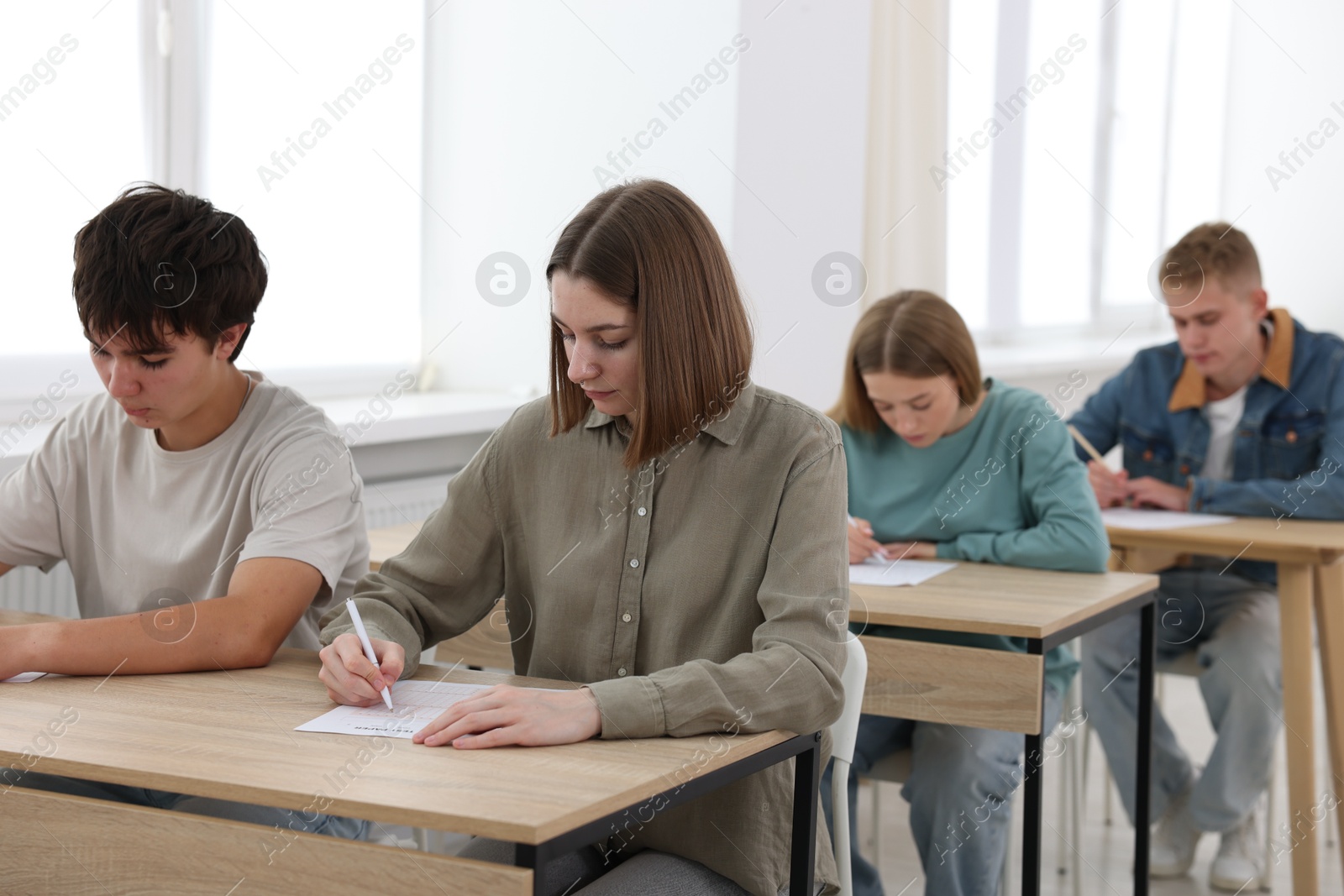 Photo of Students taking exam at wooden table indoors, selective focus