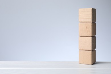 Photo of Blank cubes on white wooden table against light grey background, space for text