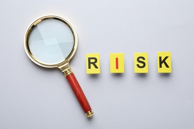 Photo of Word Risk and magnifying glass on light grey background, flat lay