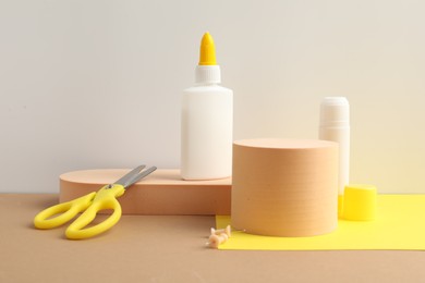 Photo of Glue in bottle, stick, scissors and pins on beige table against light grey background, closeup