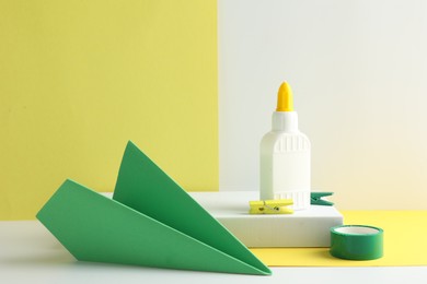 Photo of Glue in bottle, adhesive tape and green paper plane on color background, closeup